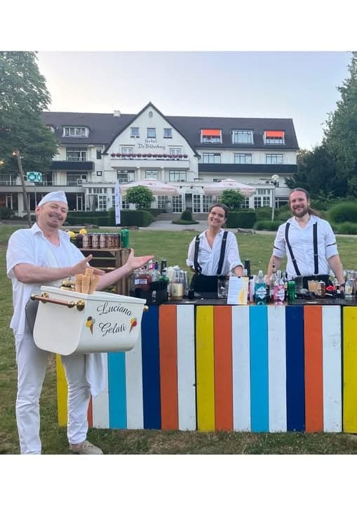 Luciano Gelati met zijn mobiele ijsbak naast een gekleurde bar met twee barmedewerkers op het gazon voor Hotel de Bilderberg in Oosterbeek