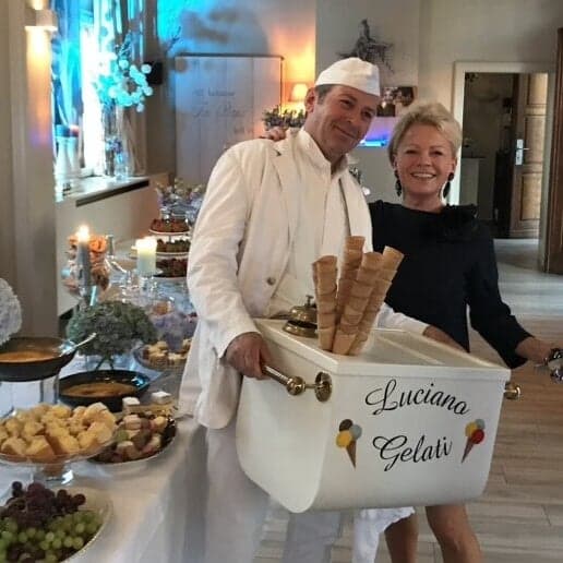 Luciano Gelati met zijn mobiele ijsbak en een stapel hoorntjes naast een lachende vrouw bij een gedekt buffet