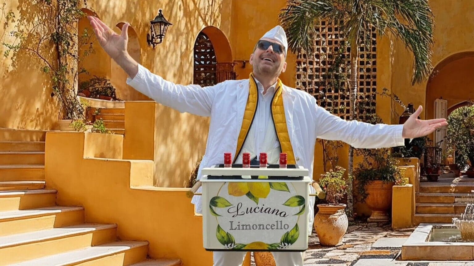 Luciano Gelati in wit kostuum op een gele Italiaanse binnenplaats, sfeer voor een Italiaanse themavond