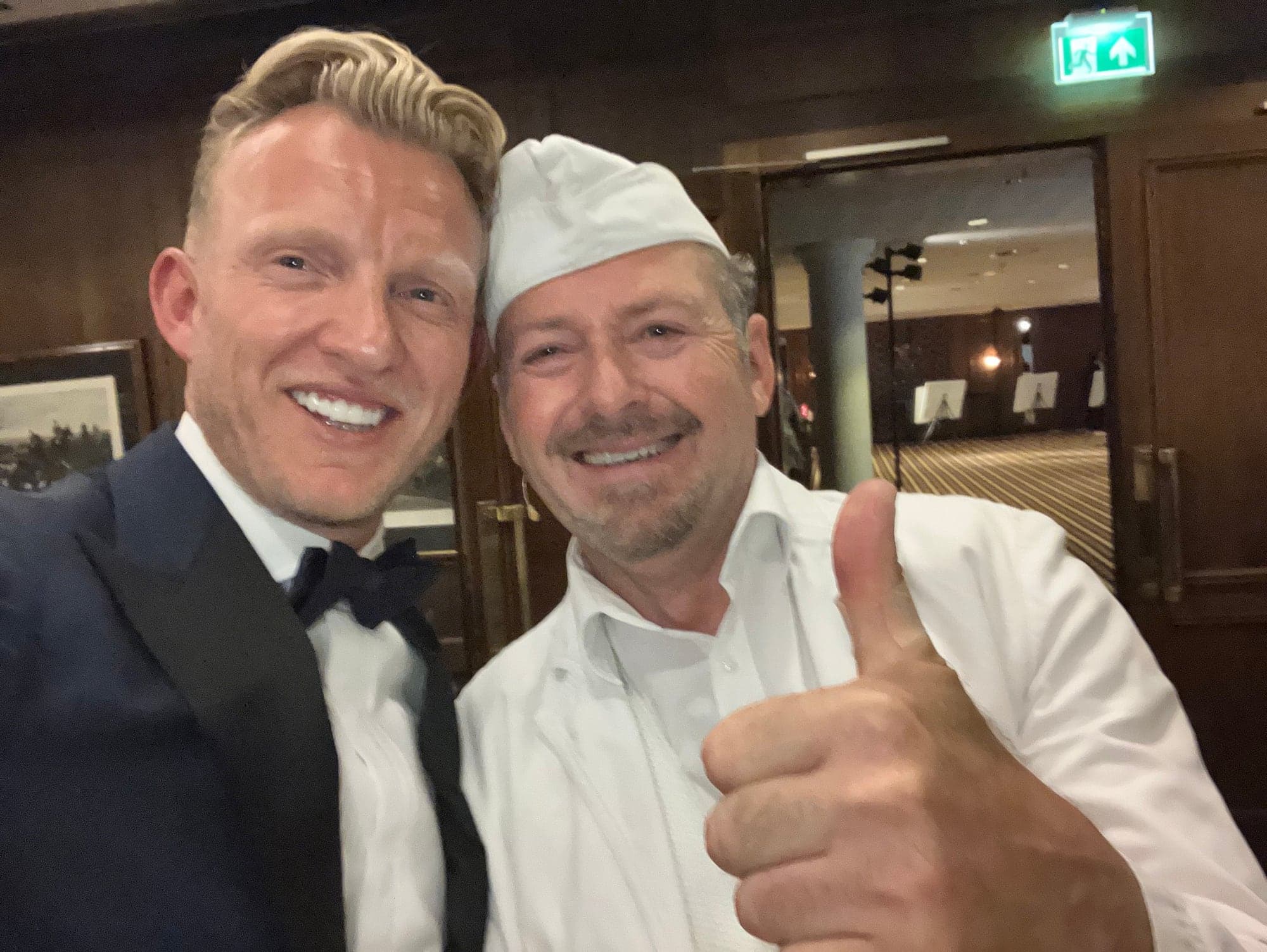 Luciano in wit kostuum maakt binnen een selfie met een gast in smoking