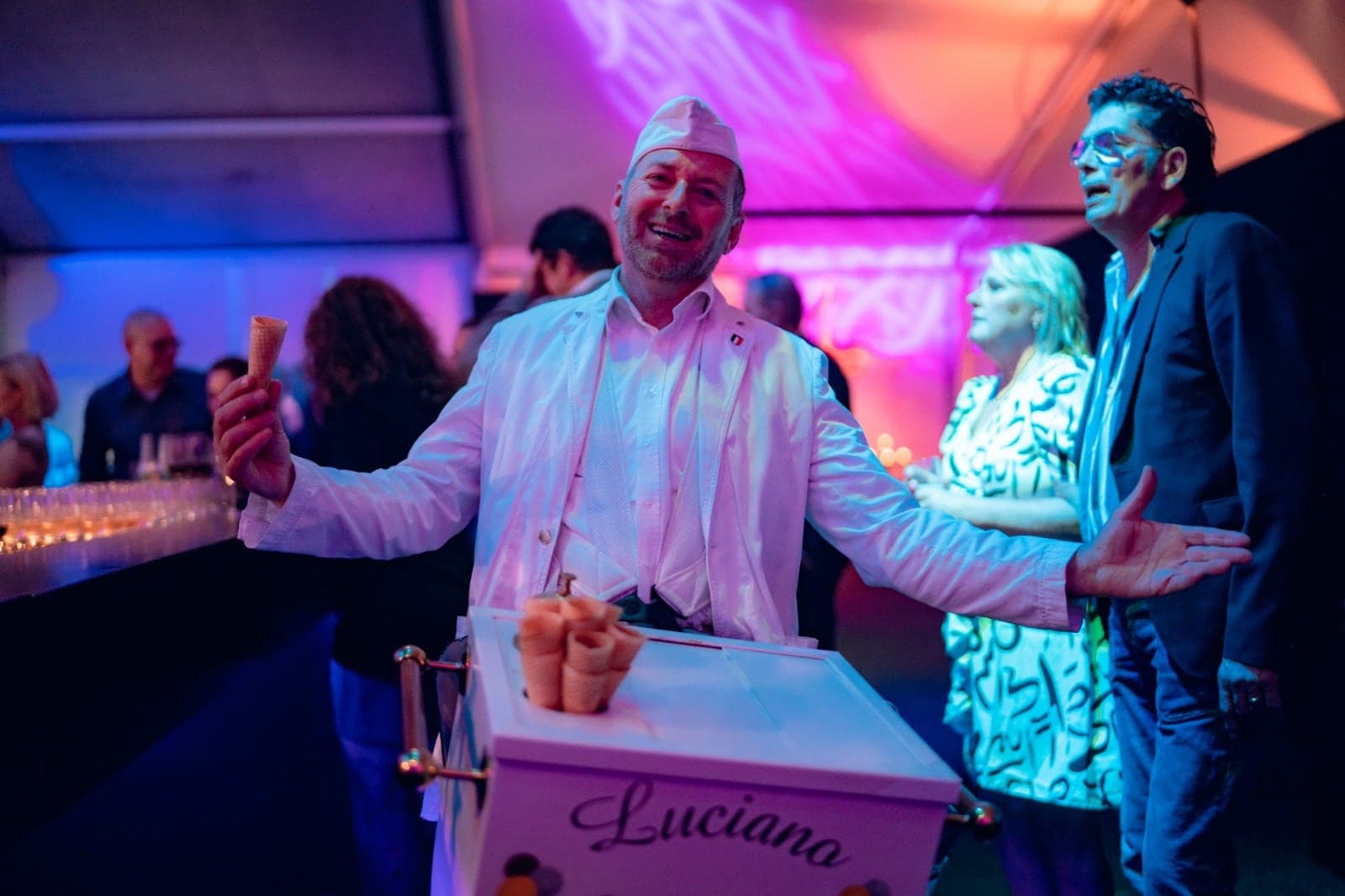 Luciano zingt met armen wijd op een bedrijfsfeest in paars licht